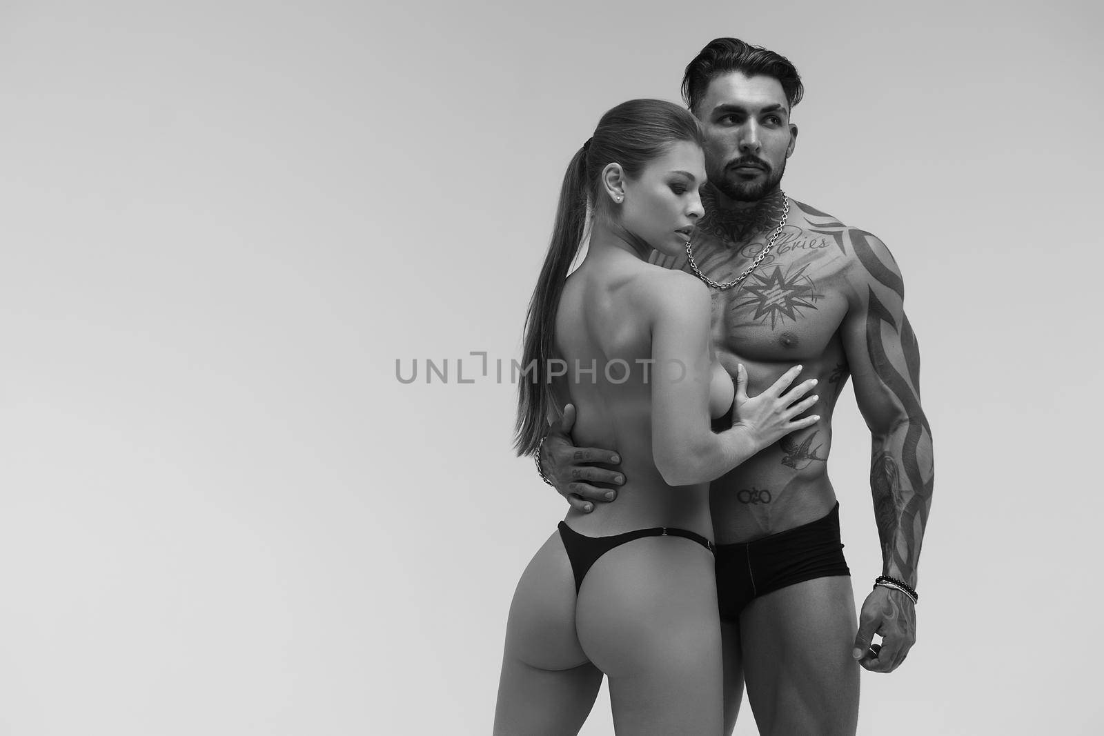 Black and white tattooed shirtless man and seductive topless woman looking away