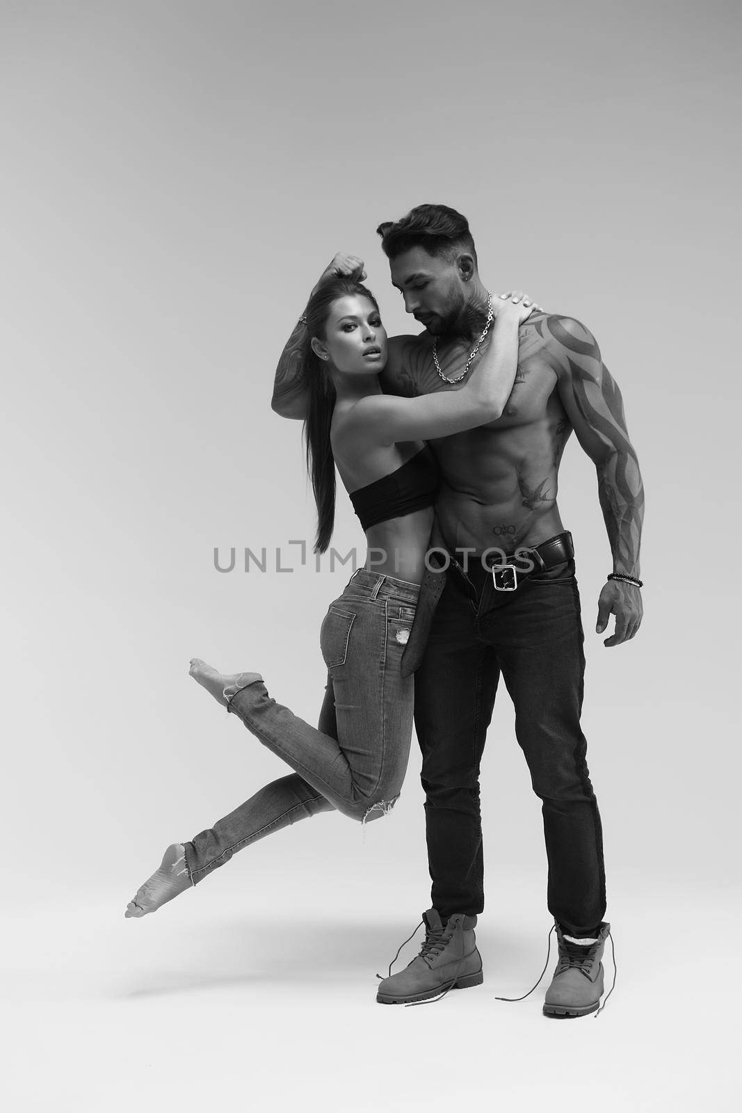 Black and white side view of topless woman and shirtless man looking at camera against gray background