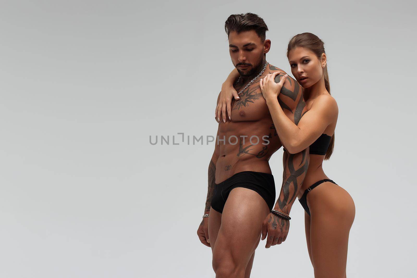 Muscular tattooed man embracing slim topless woman in panties on gray background