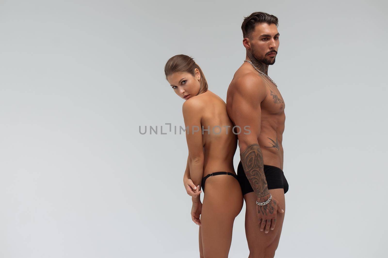 Muscular tattooed man embracing slim topless woman in panties on gray background