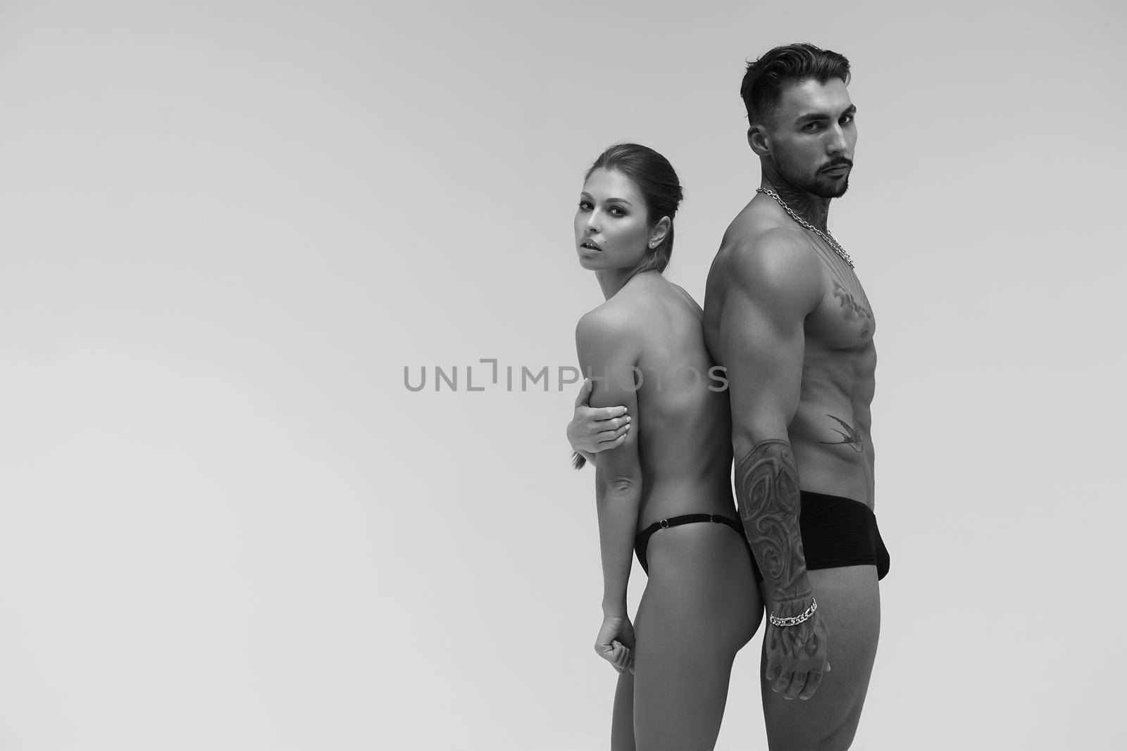 Black and white tattooed shirtless man and seductive topless woman looking away