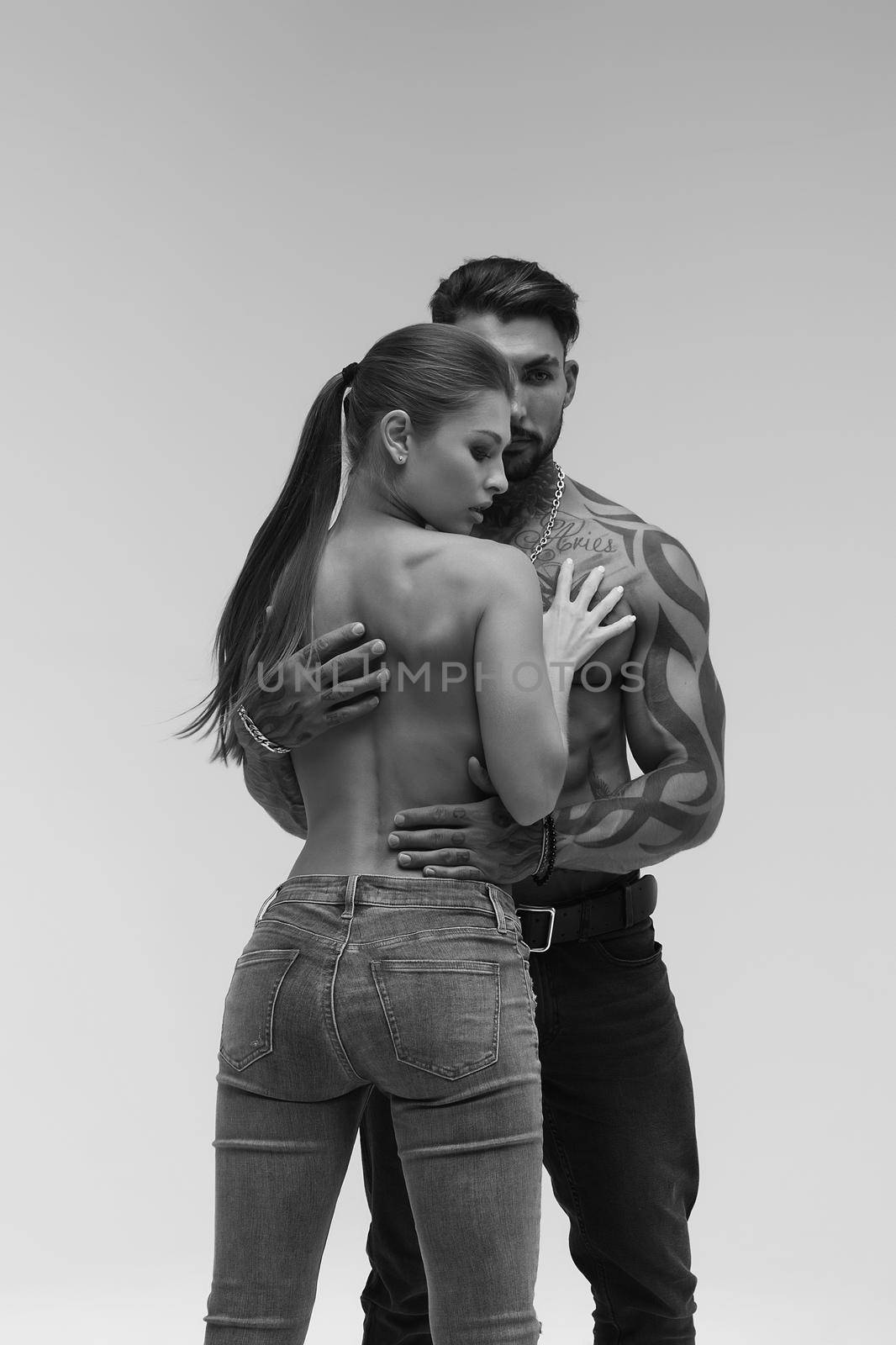 Black and white side view of topless woman and shirtless man looking at camera against gray background