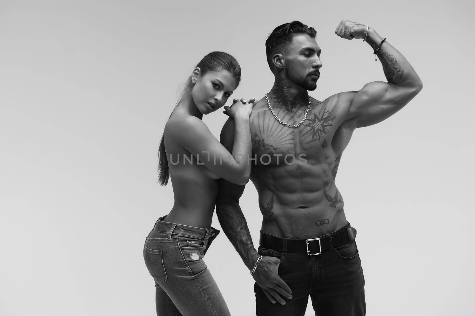 Black and white tattooed shirtless man and seductive topless woman looking away