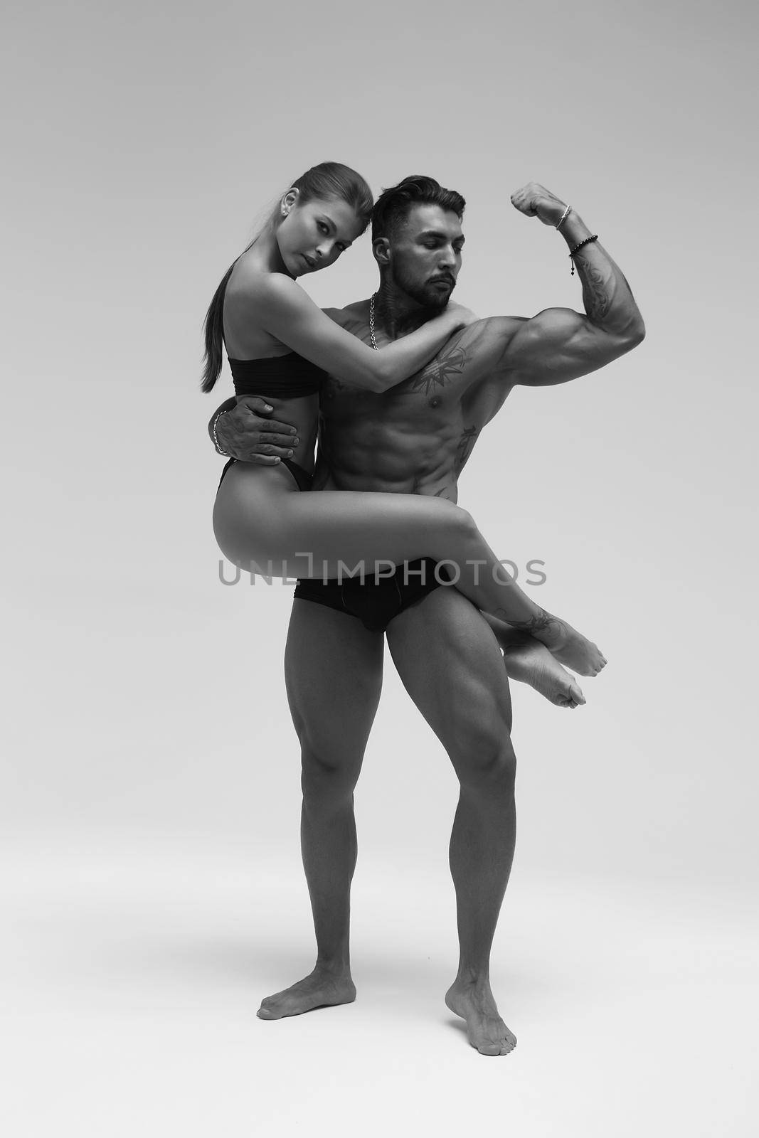 Black and white side view of topless woman and shirtless man looking at camera against gray background