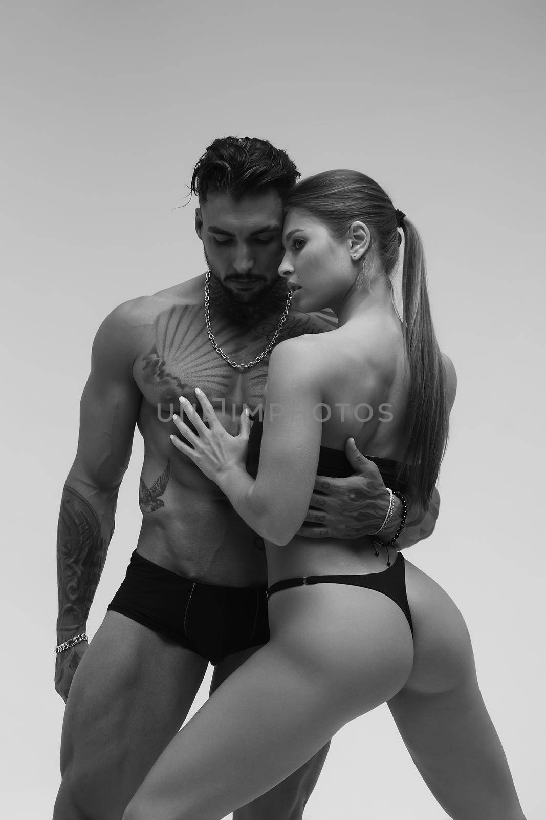 Black and white side view of topless woman and shirtless man looking at camera against gray background