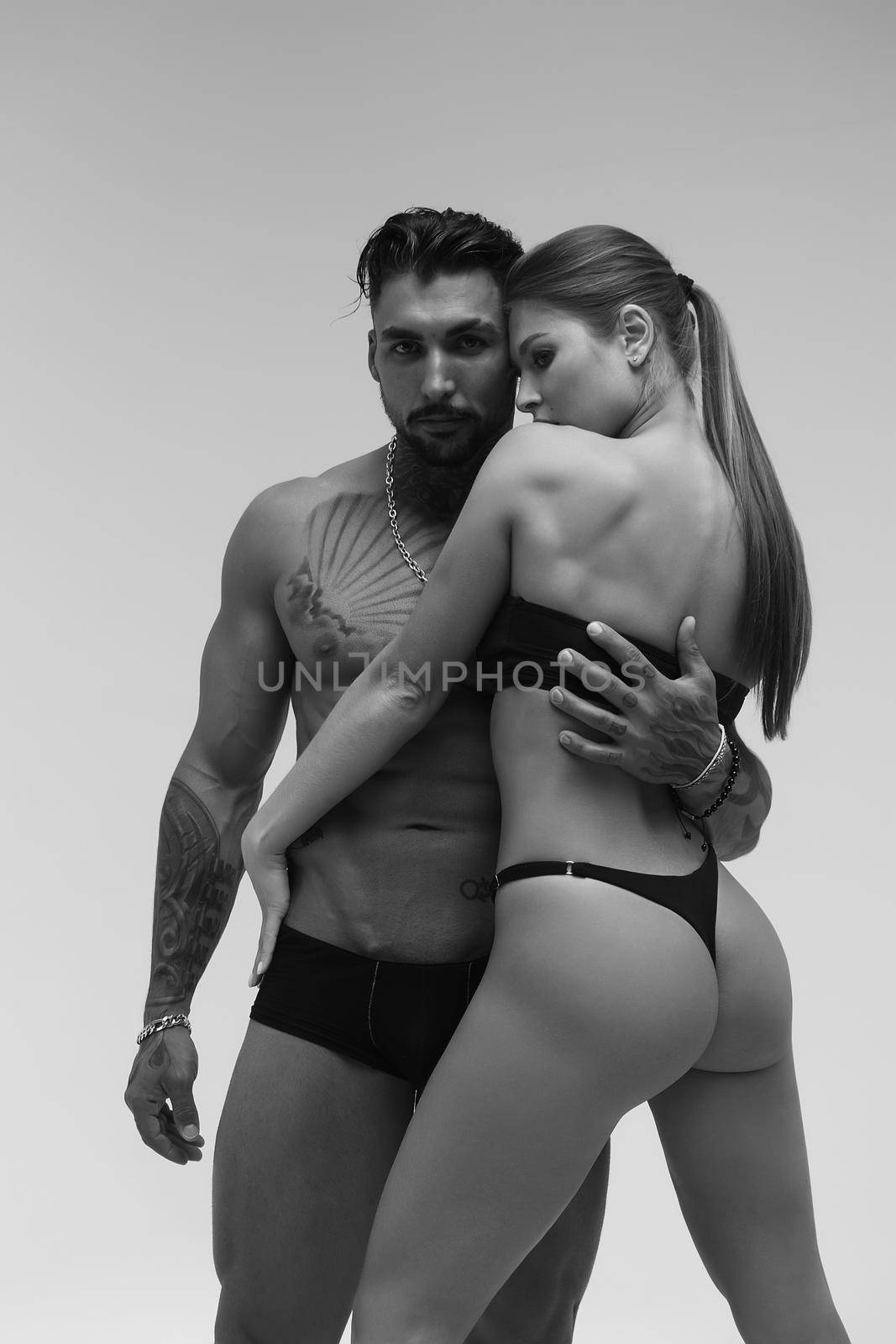 Black and white side view of topless woman and shirtless man looking at camera against gray background