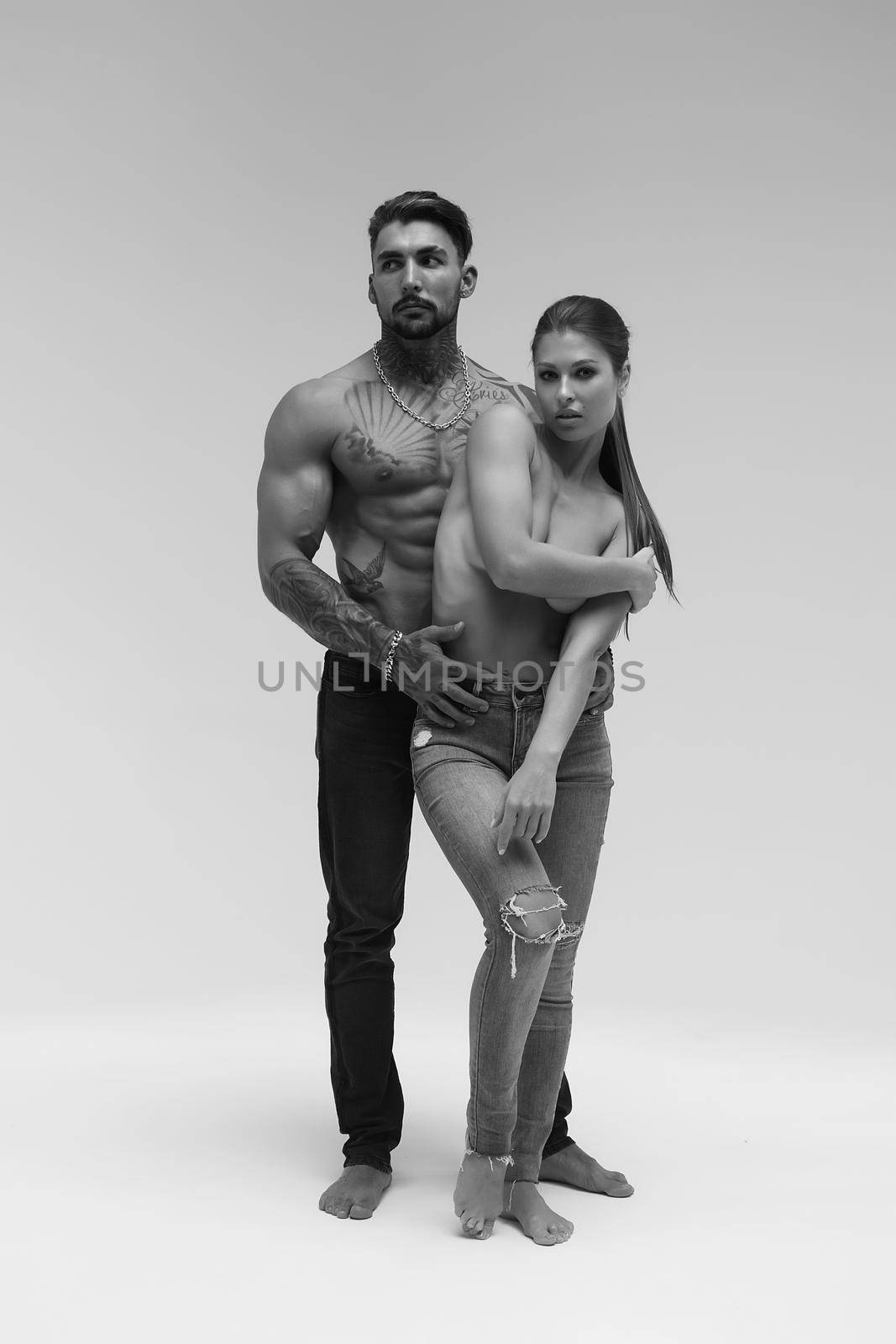 Black and white side view of topless woman and shirtless man looking at camera against gray background