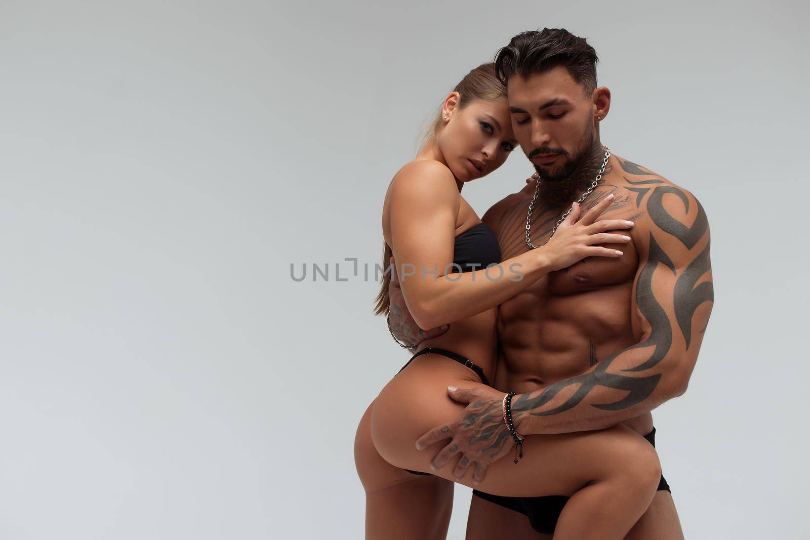 Strong shirtless male embracing and covering breast of attractive topless female on gray background