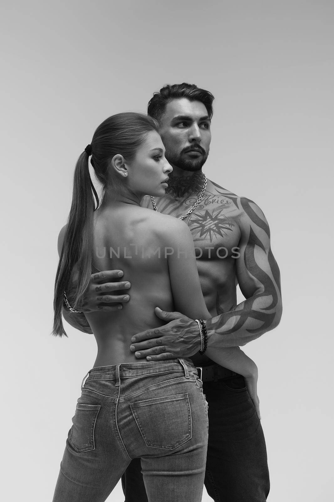 Black and white side view of topless woman and shirtless man looking at camera against gray background