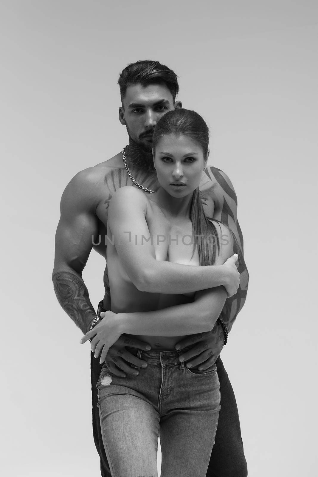 Black and white side view of topless woman and shirtless man looking at camera against gray background