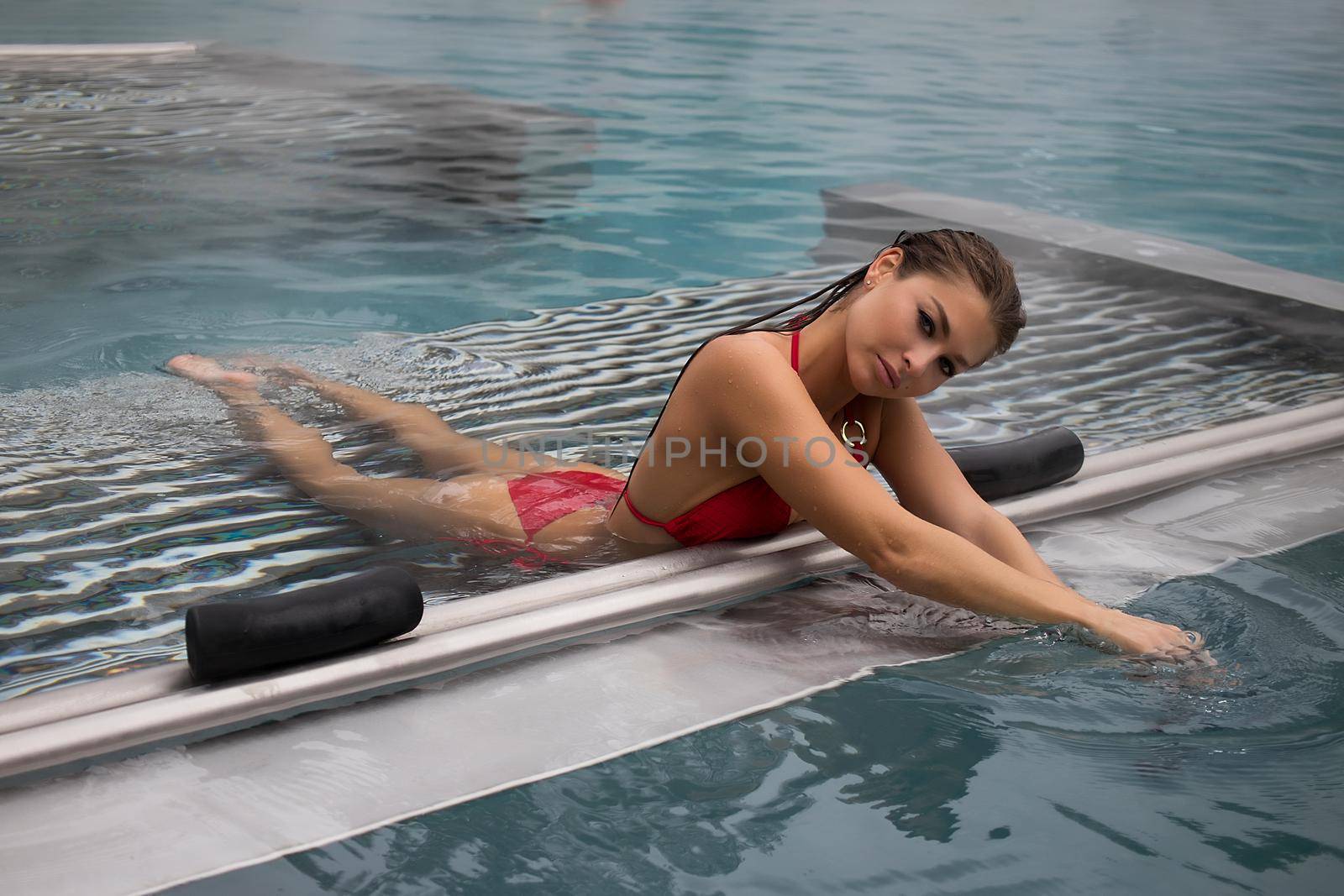 Sexy barefoot female in red swimsuit lying on grates in water of hot spring on resort