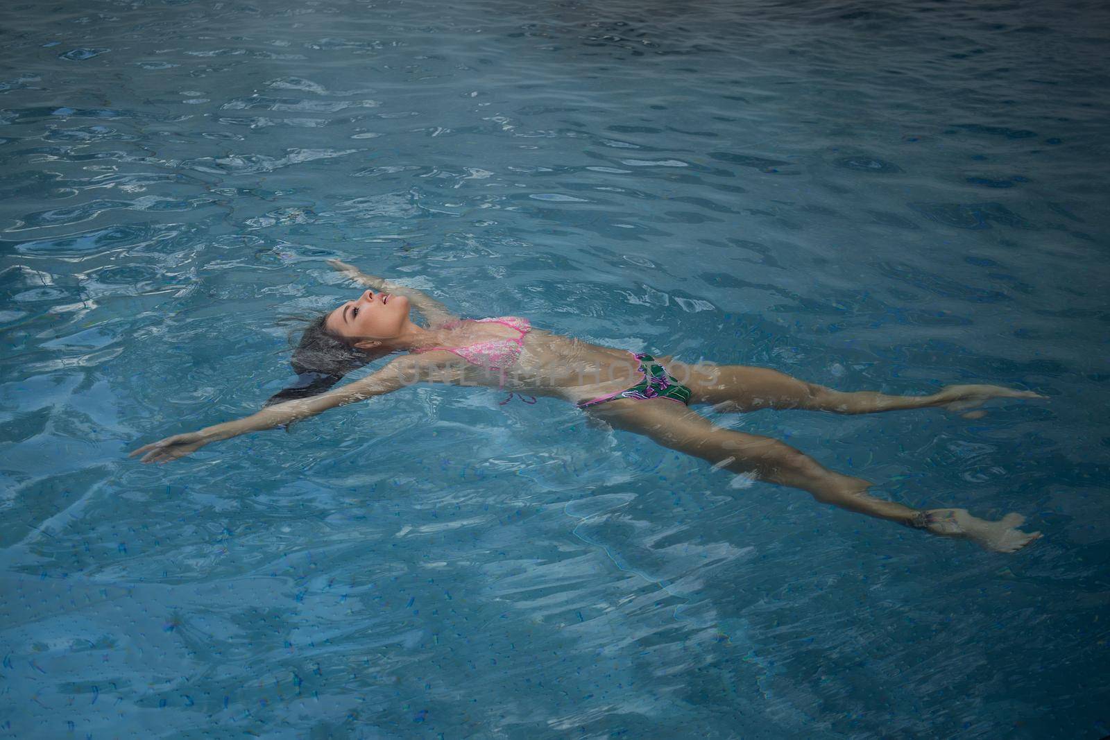 From above seductive woman touching wet hair and net while resting in clean pool water on resort