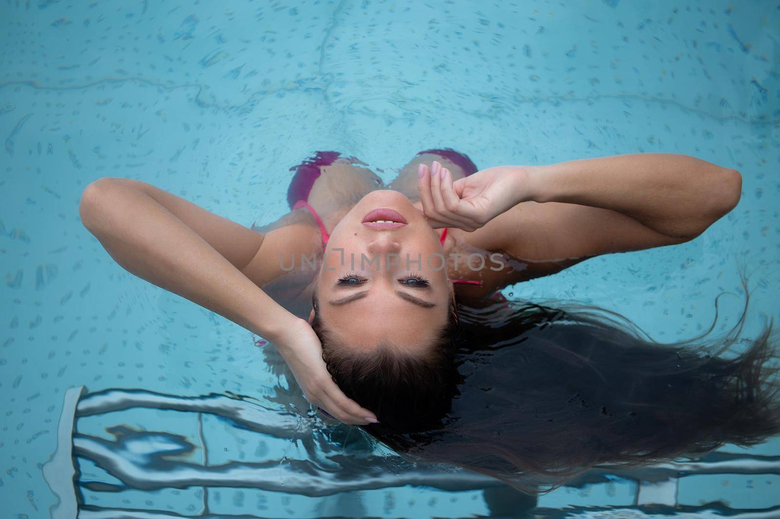 From above seductive woman touching wet hair and net while resting in clean pool water on resort