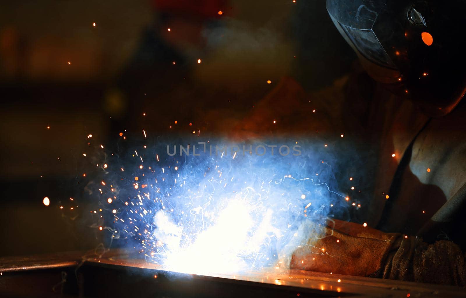 Welder at work. Welding of metal sparks and smoke in the workshop. Industrial Welder With gas Torch in Protective Helmet, welding metal profiles. The welding operation at construction site.