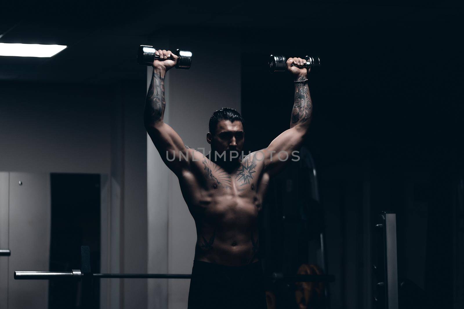 Strong male bodybuilder doing exercises with dumbbells by 3KStudio