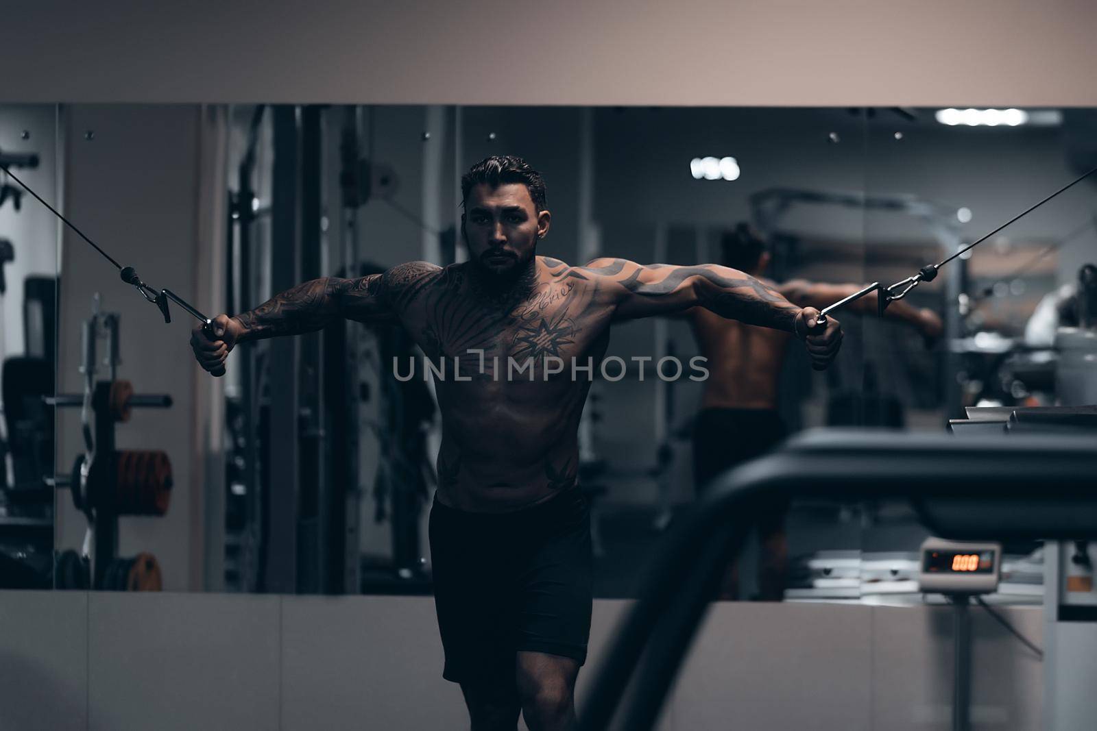 Strong male bodybuilder doing exercises with dumbbells by 3KStudio