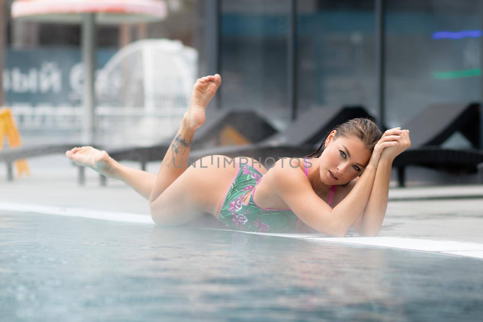 Sexy barefoot female in green swimsuit lying on grates in water of hot spring on resort