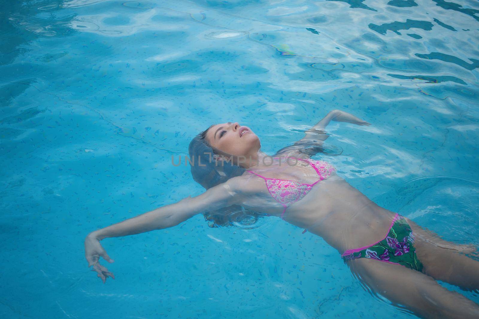 From above seductive woman touching wet hair and net while resting in clean pool water on resort