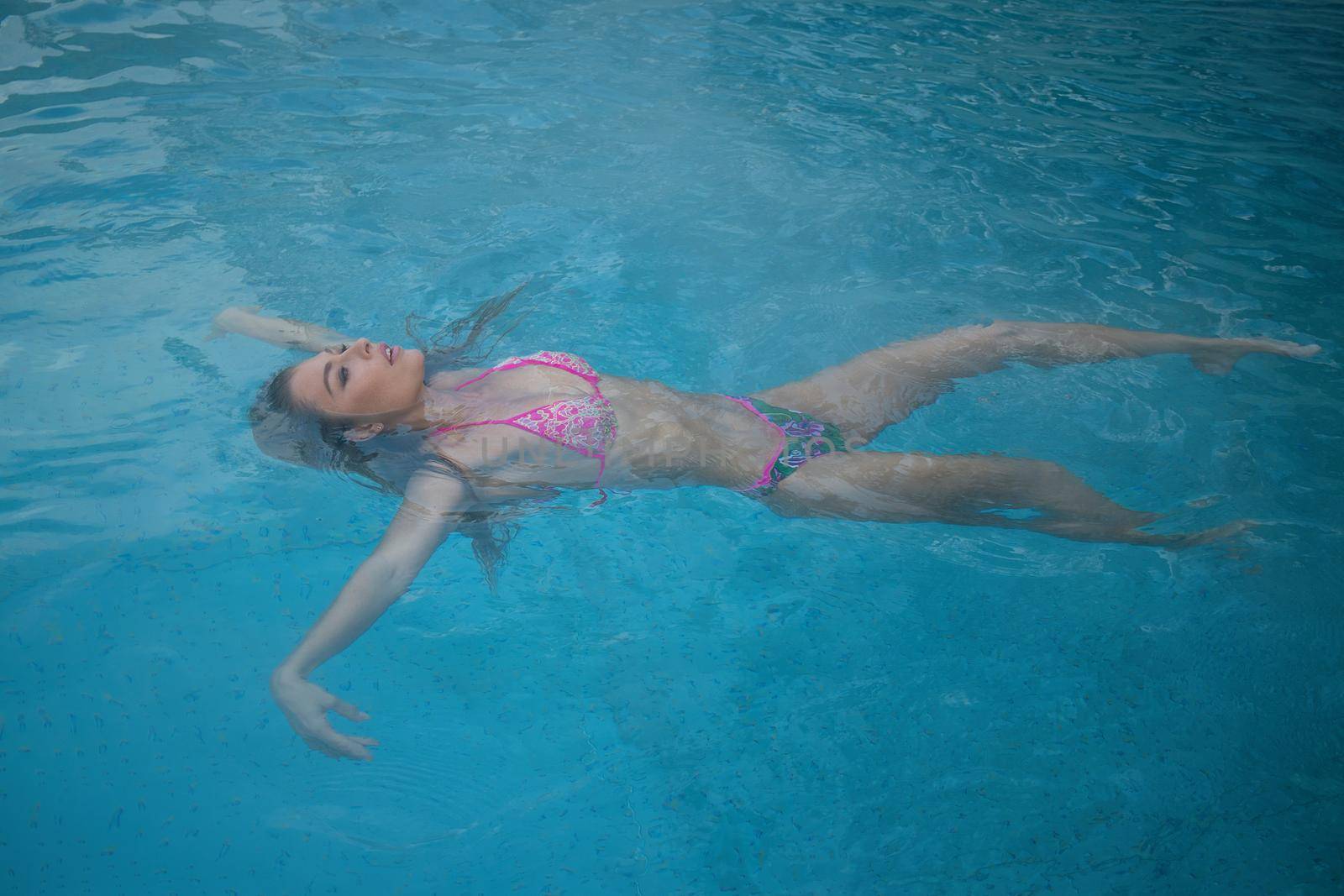 From above seductive woman touching wet hair and net while resting in clean pool water on resort