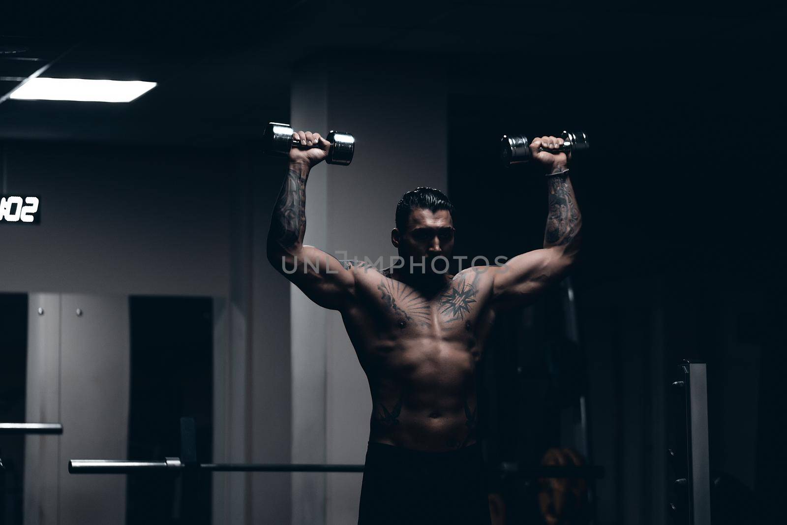 Strong male bodybuilder doing exercises with dumbbells by 3KStudio