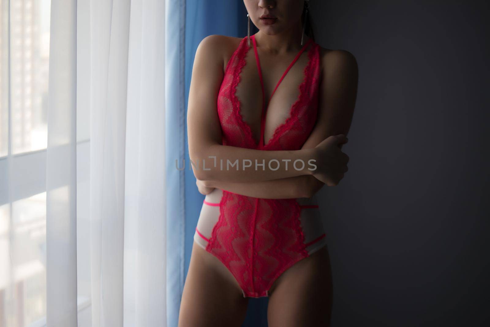 Alluring woman in red underwear standing near window by 3KStudio