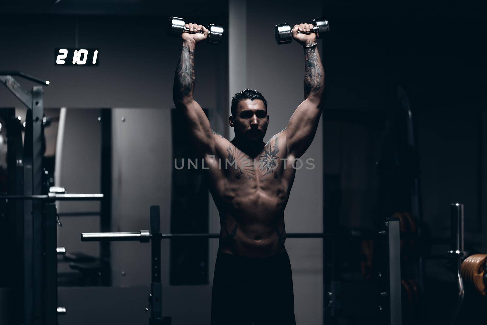 Strong male bodybuilder doing exercises with dumbbells by 3KStudio