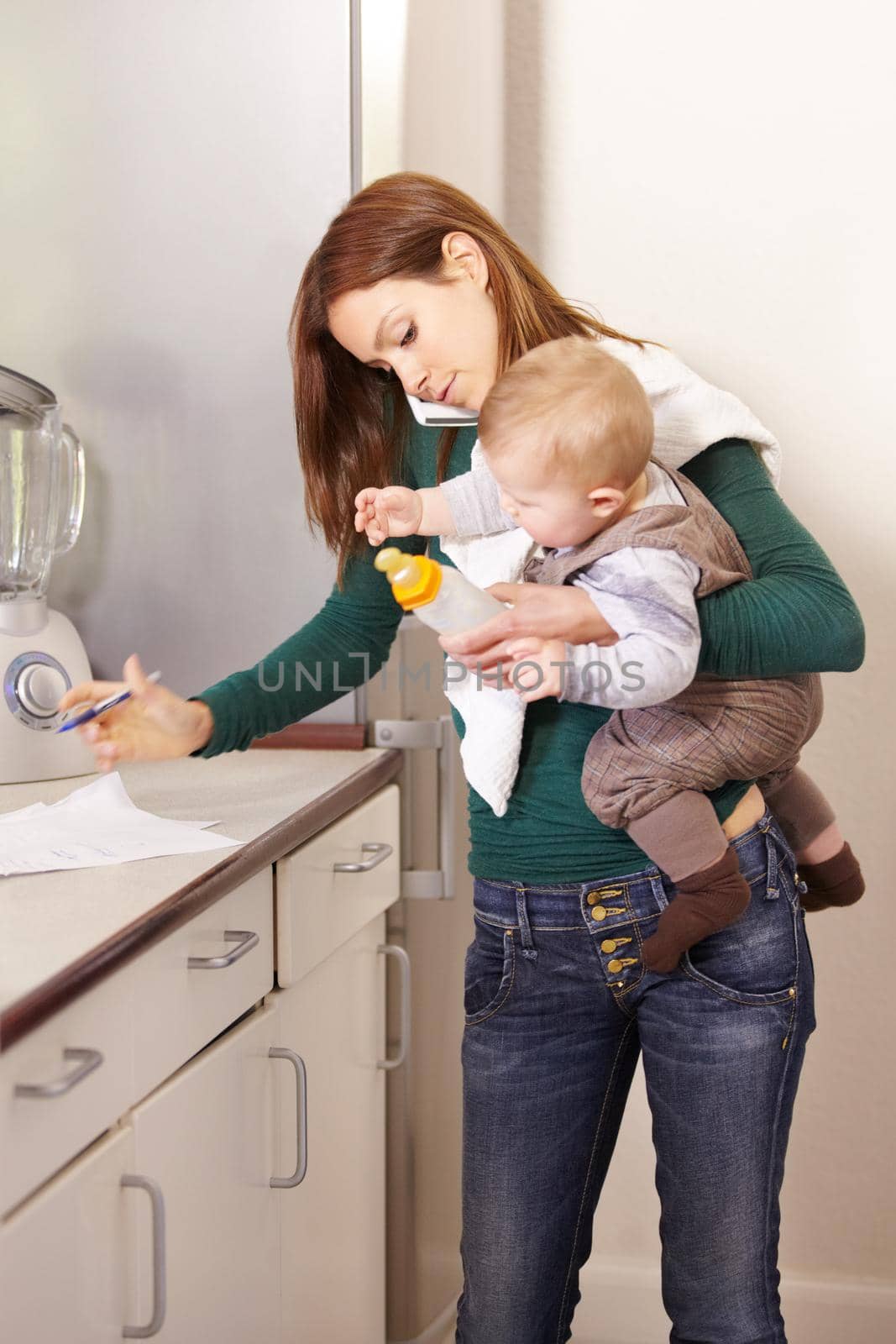 Young mom trying to multi-task while holding her baby son and his bottle.