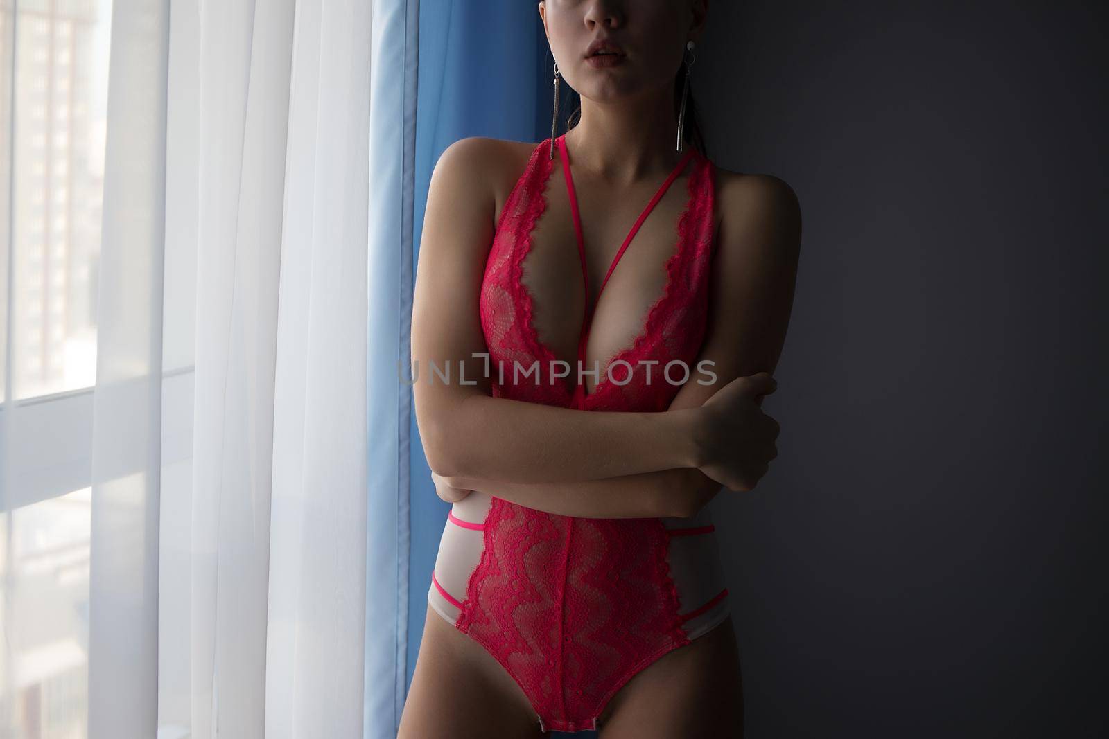 Alluring woman in red underwear standing near window by 3KStudio