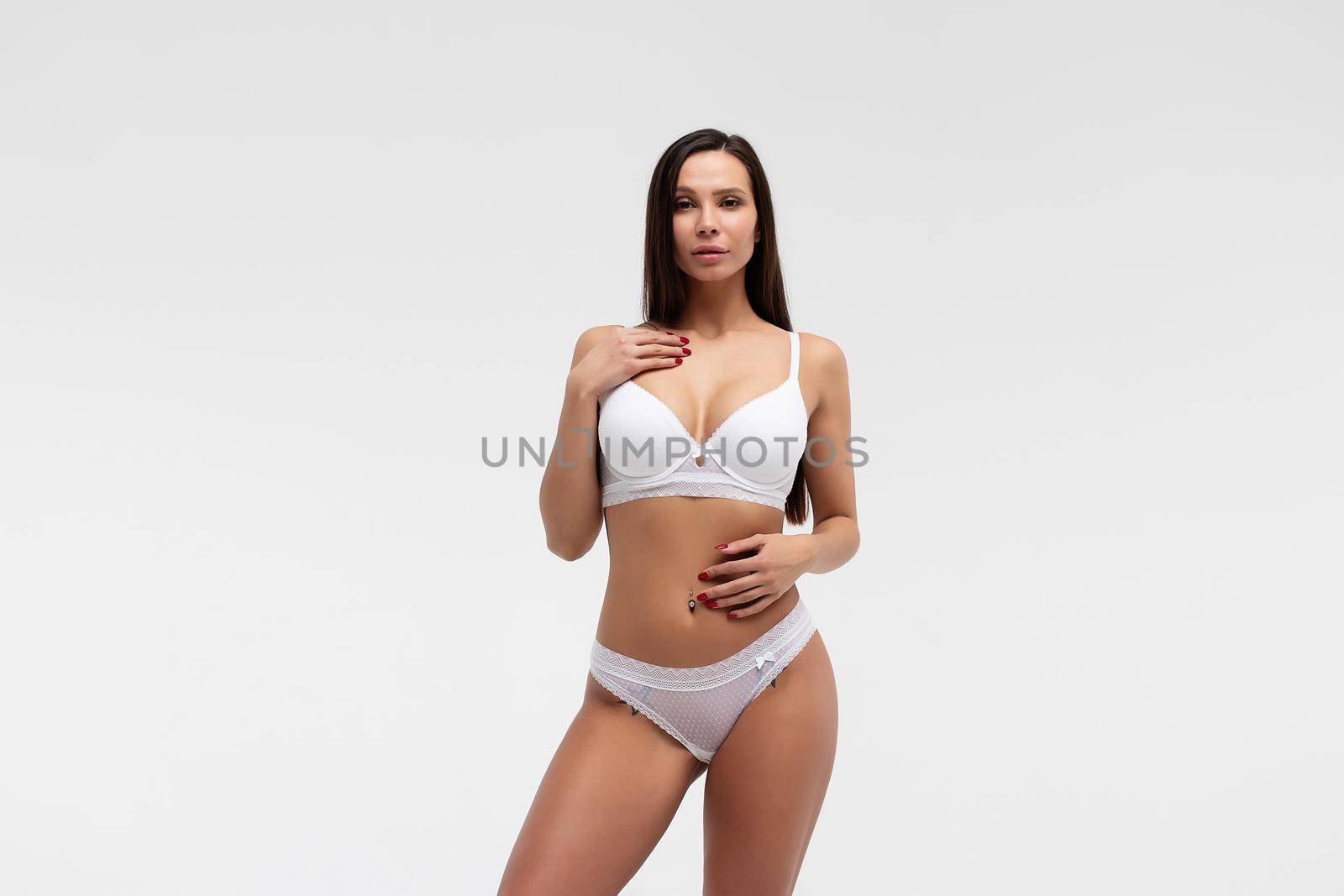 Confident female wearing white underwear standing with hands on waist on white background and looking at camera