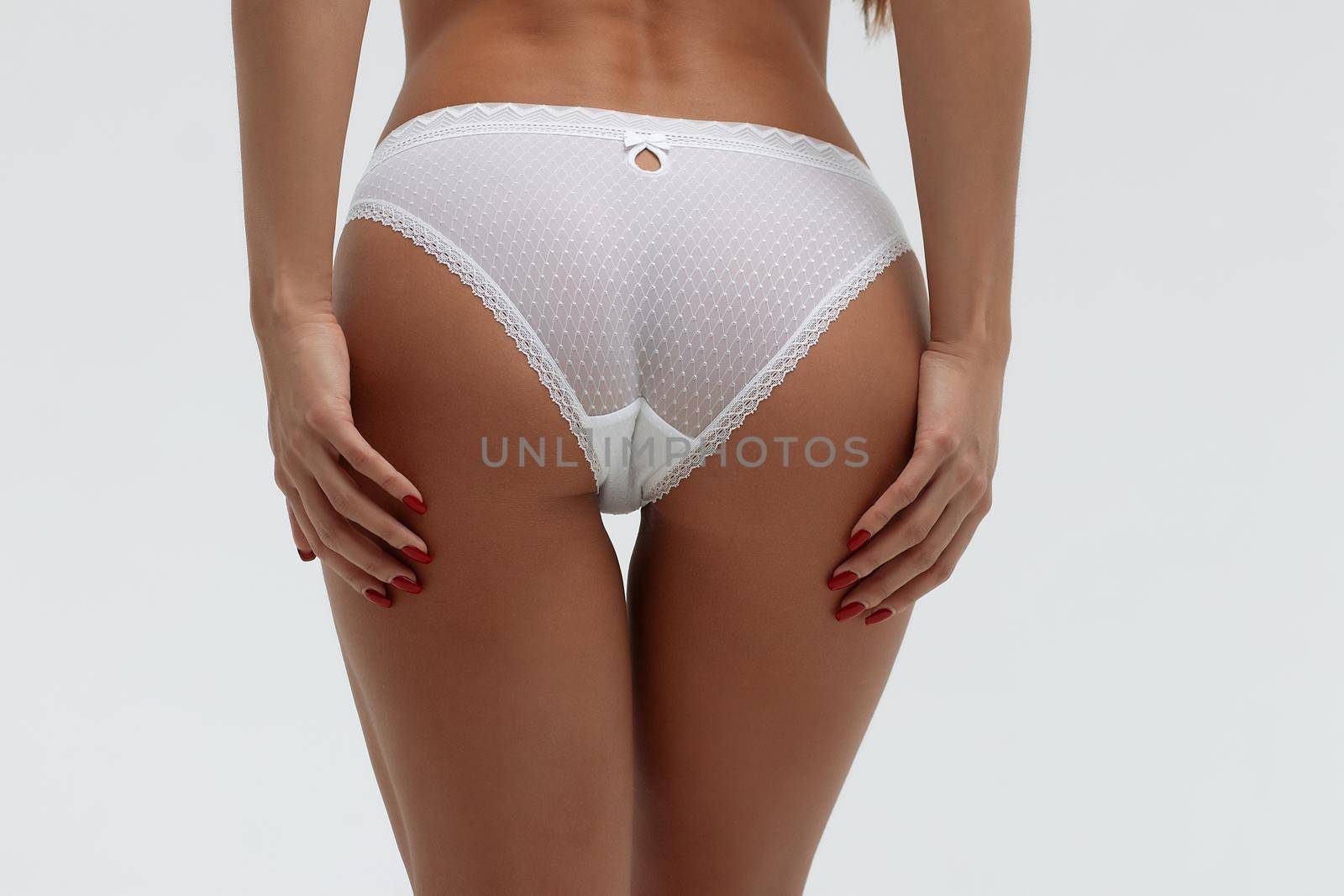 Back view of unrecognizable slim female wearing white lingerie standing on white background in studio