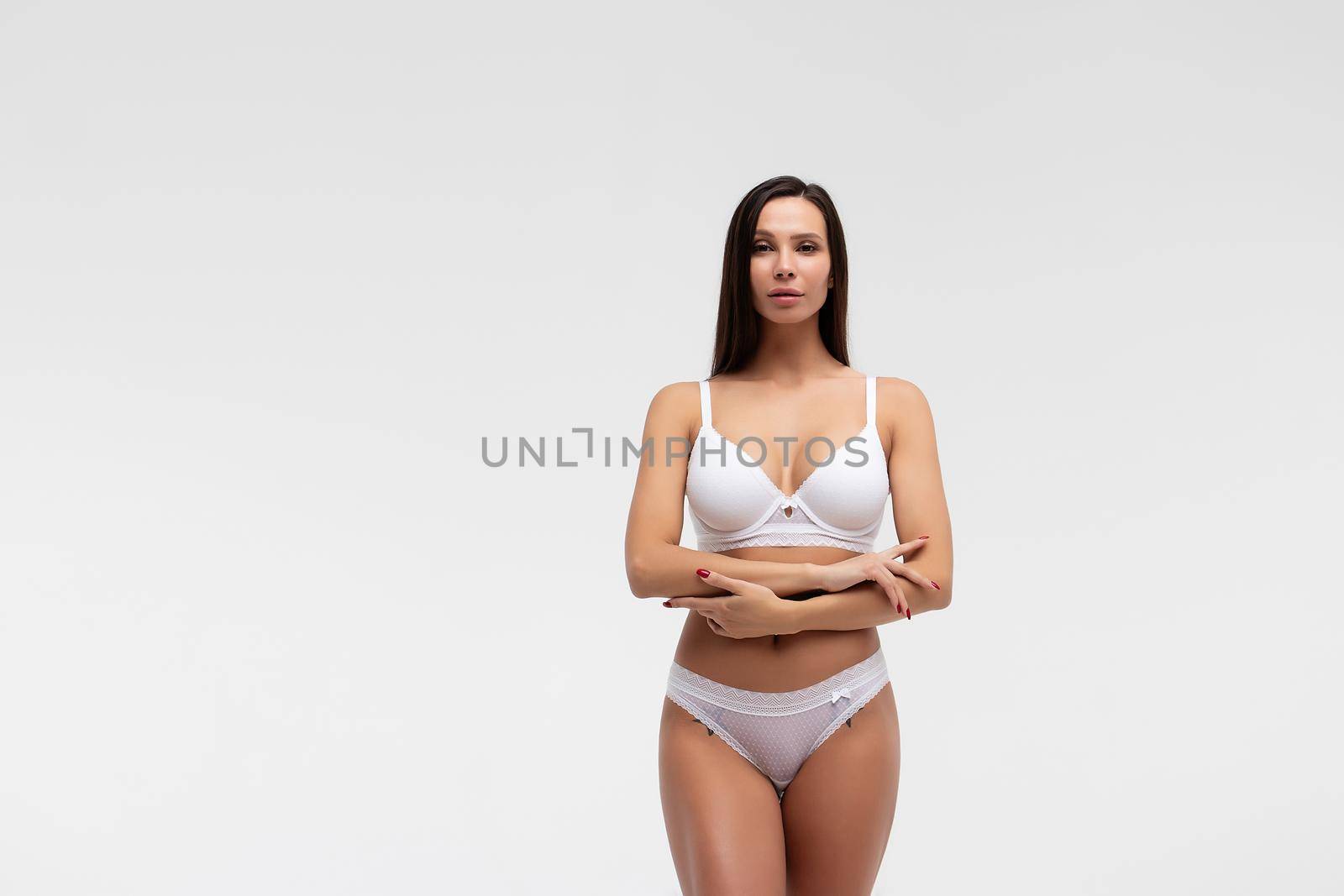 Confident female wearing white underwear standing with hands on waist on white background and looking at camera