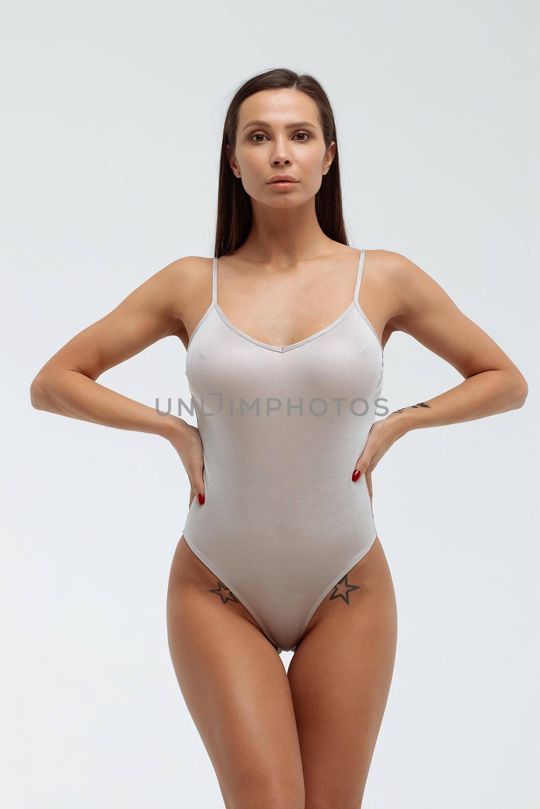 Tender female wearing bodysuit standing with folded arms on white background in studio and looking away