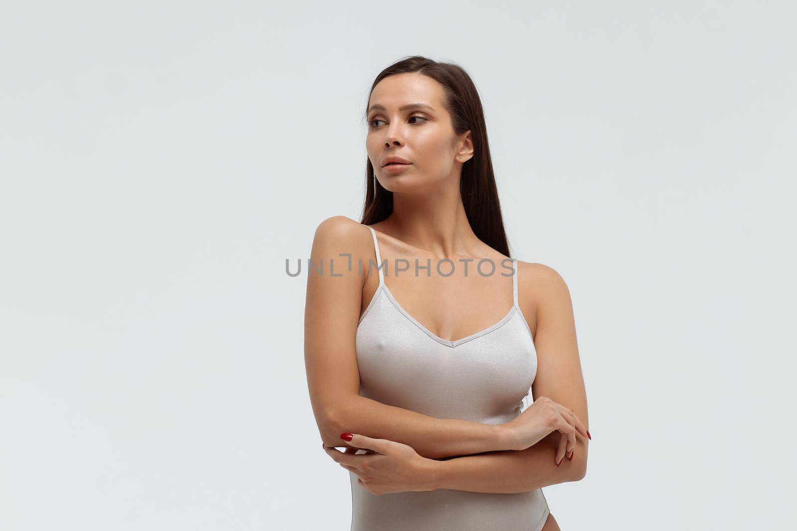 Tender female wearing bodysuit standing with folded arms on white background in studio and looking away