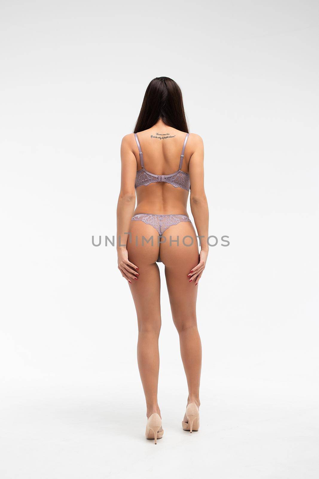 Back view of unrecognizable slim female wearing purple lingerie standing on white background in studio