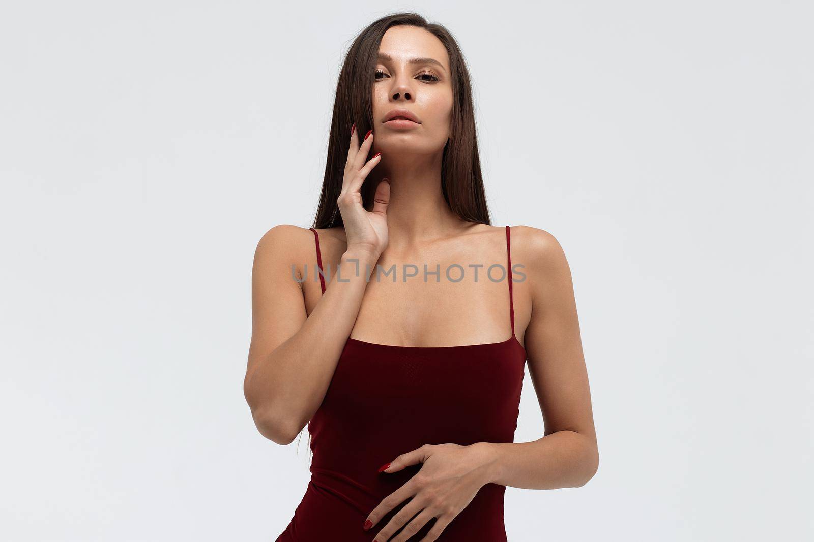 Sexy young female wearing red bodysuit and high heeled shoes standing on white background in studio and looking at camera