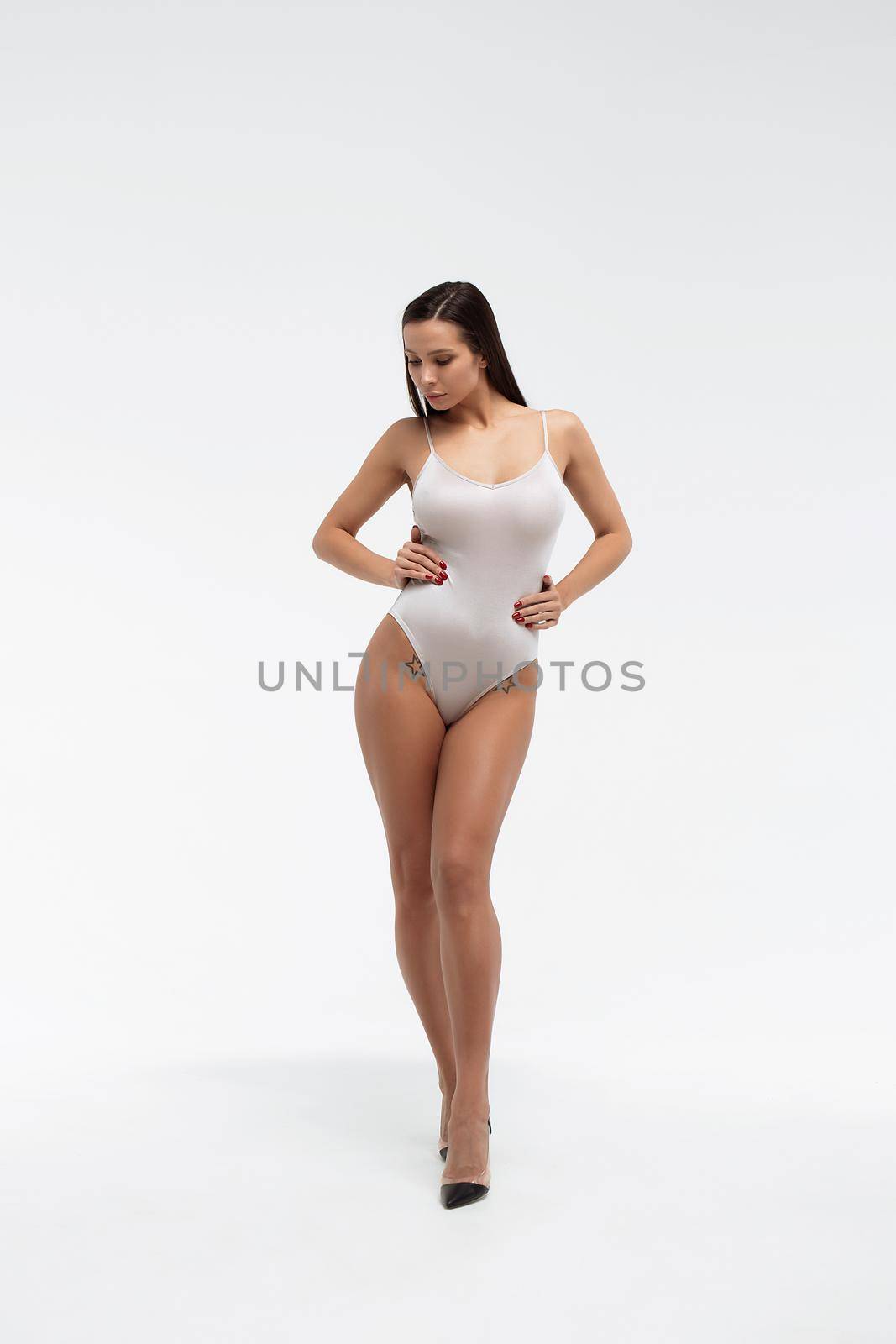 Tender female wearing bodysuit standing with folded arms on white background in studio and looking away