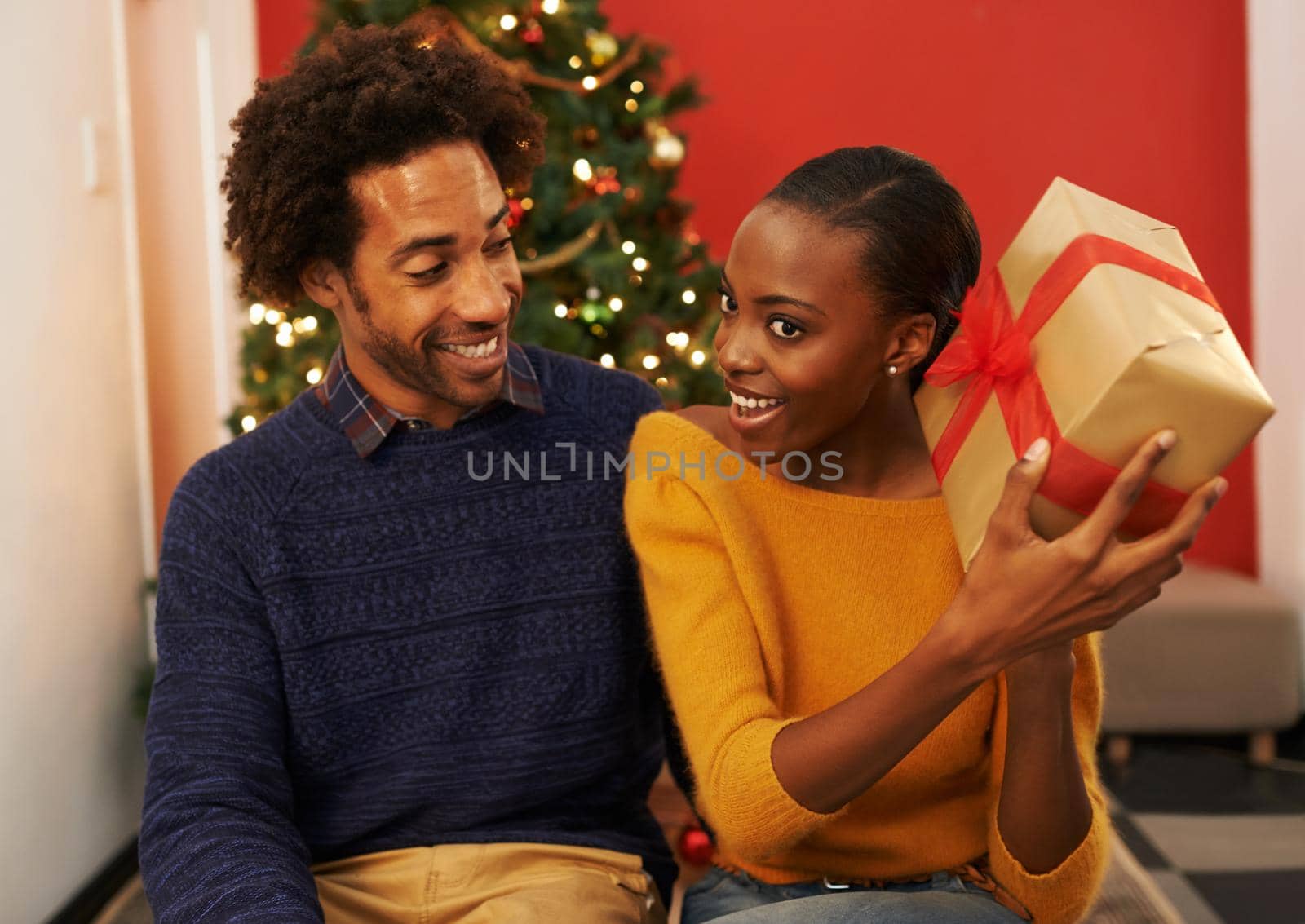 Shot of a young woman holding up her Christmas present while sitting beside her boyfriend.