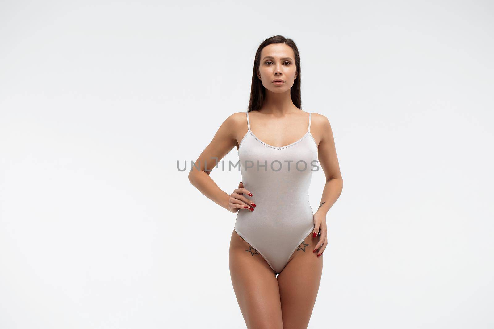 Tender female wearing bodysuit standing with folded arms on white background in studio and looking away