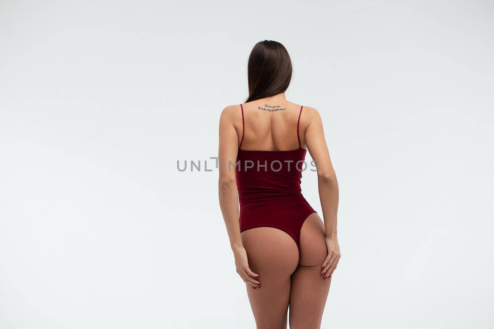 Back view of unrecognizable slim female wearing beige lingerie standing on white background in studio