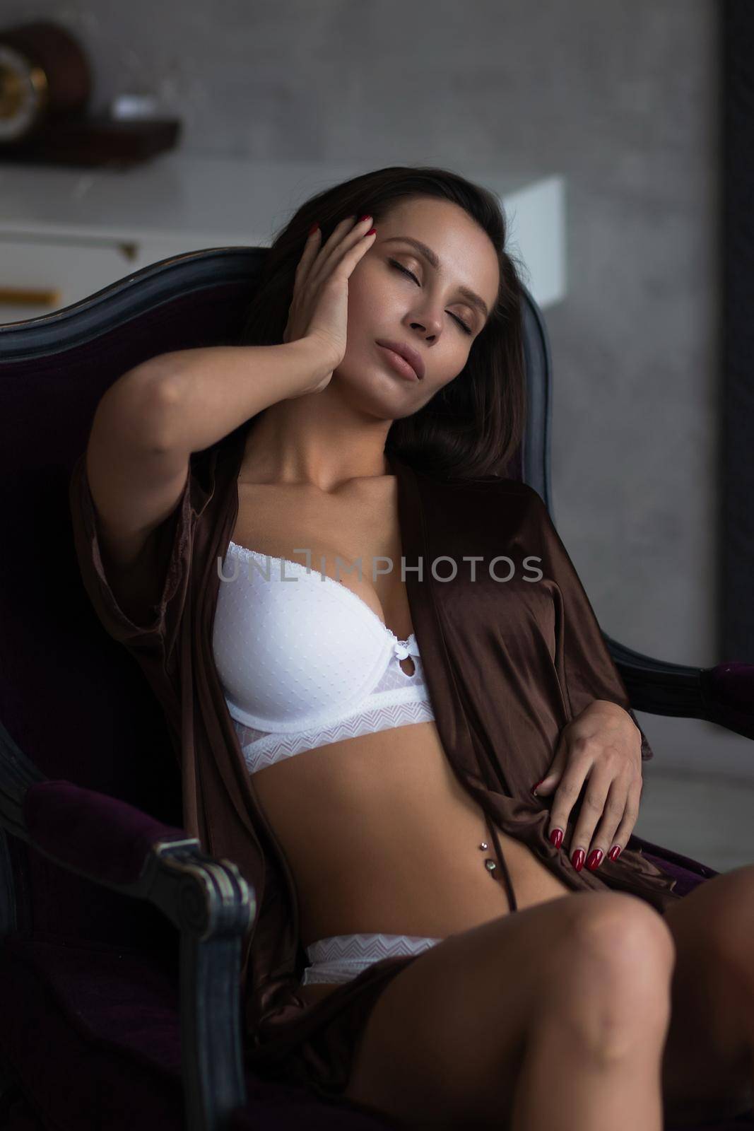 Sensual young female with long dark hair in stylish dress with decollete relaxing in comfortable armchair and looking away