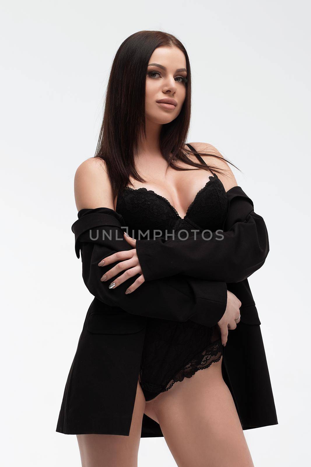 Young slim seductive woman with makeup in black underwear embracing herself while looking at camera