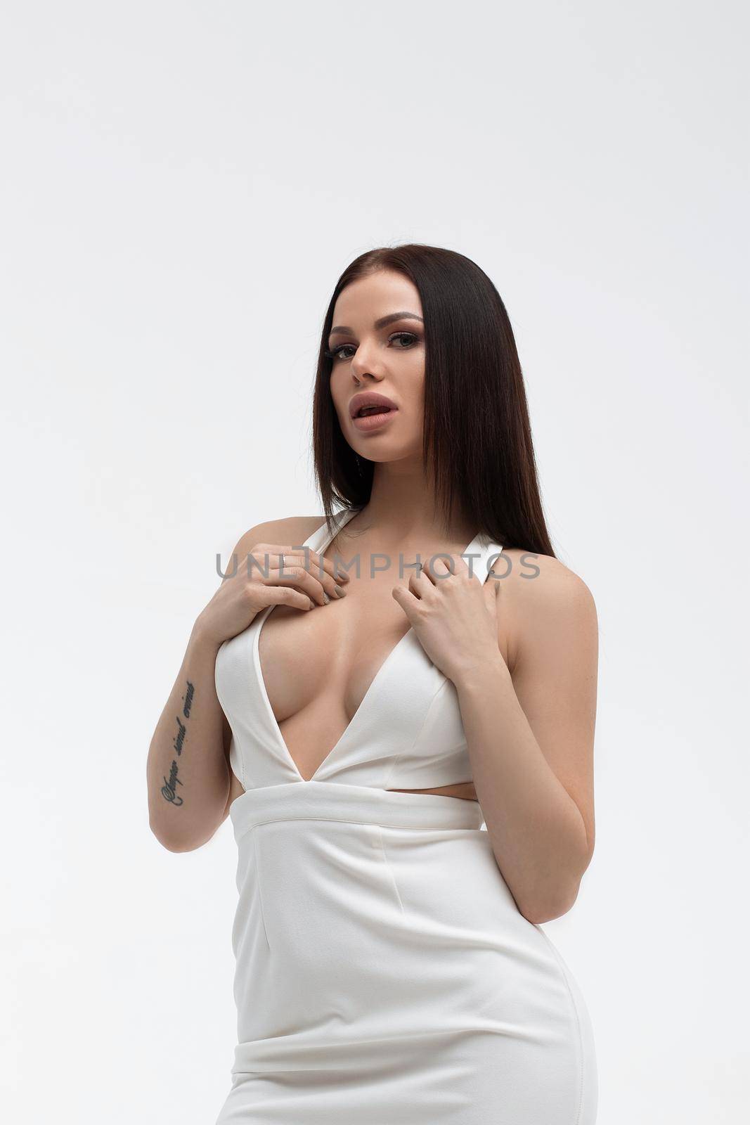 Young stylish seductive female in trendy white dress with low neckline looking erotically at camera