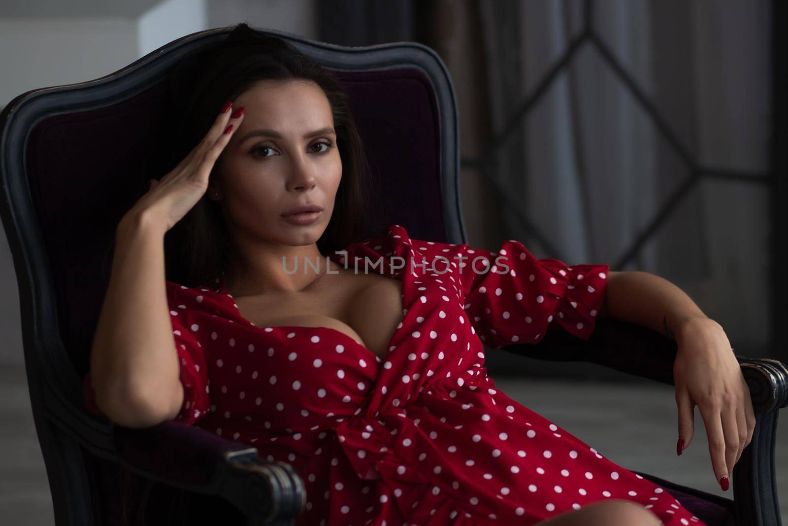 Alluring young woman in feminine dress resting in armchair by 3KStudio