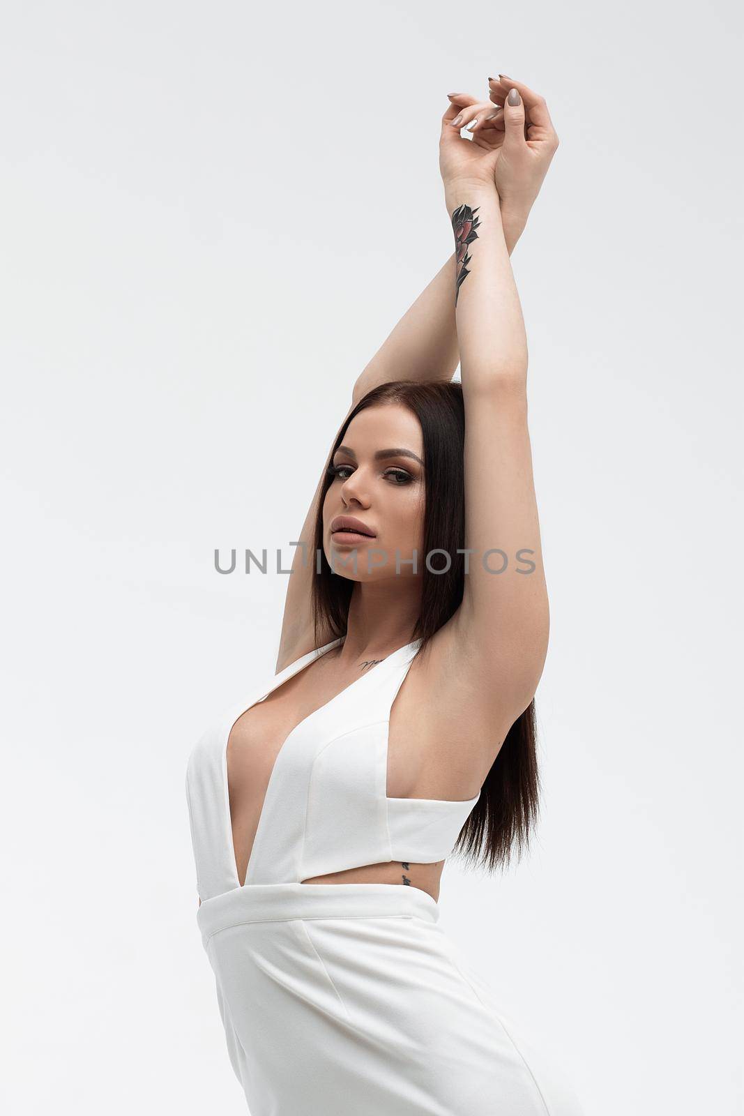 Young stylish seductive female in trendy white dress with low neckline looking erotically at camera