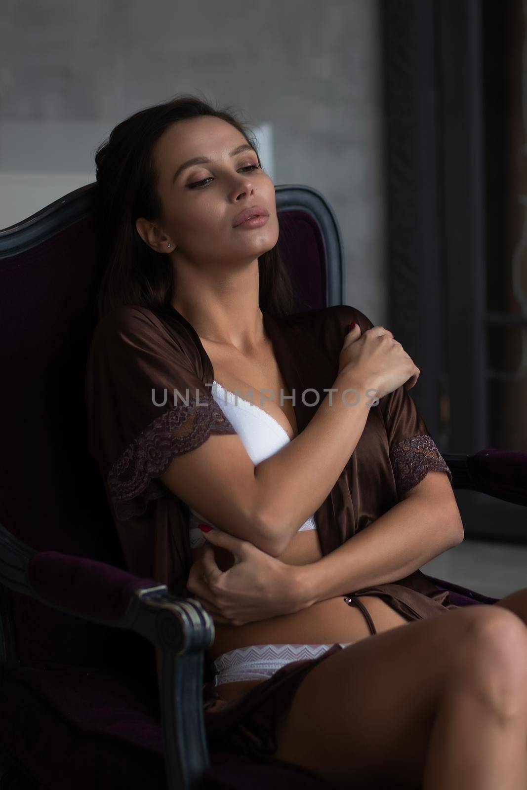 Alluring young woman in feminine dress resting in armchair by 3KStudio