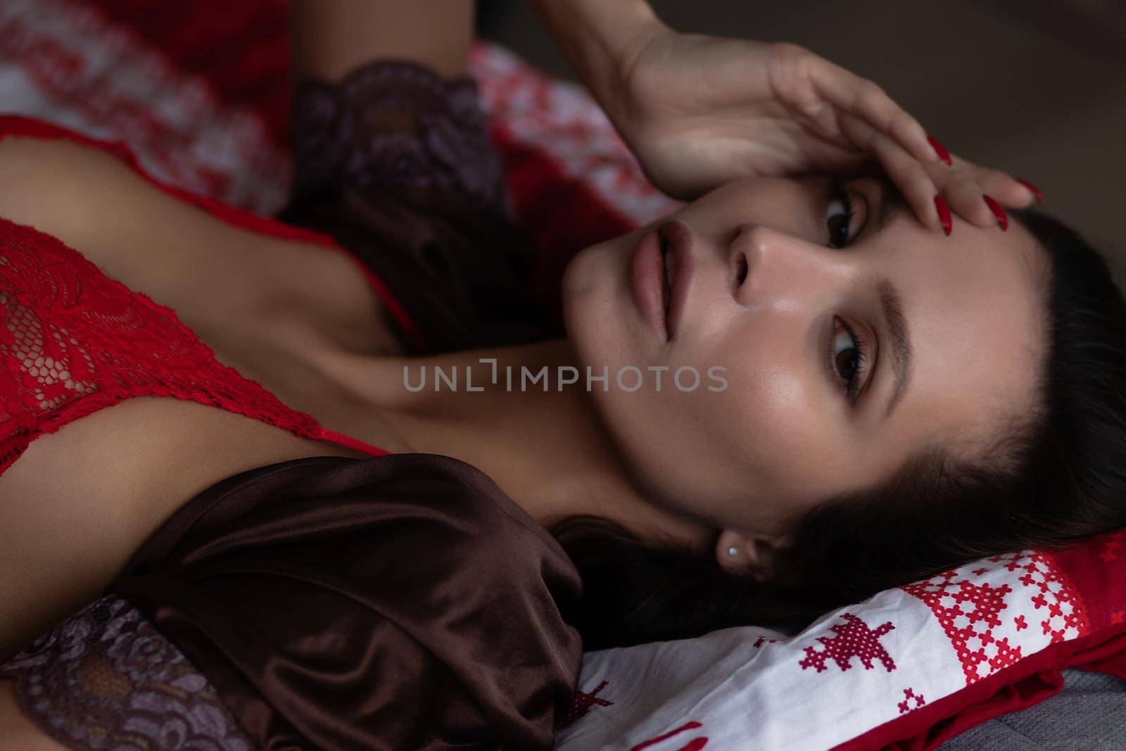 Side view of sexual young female with long dark hair in elegant red bra lying on comfortable bed with closed eyes near decorated Christmas tree