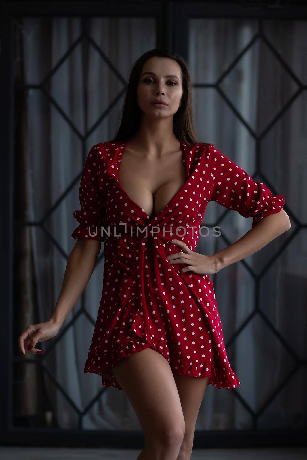 Stylish young woman in sexy dress standing with hand on waist by 3KStudio