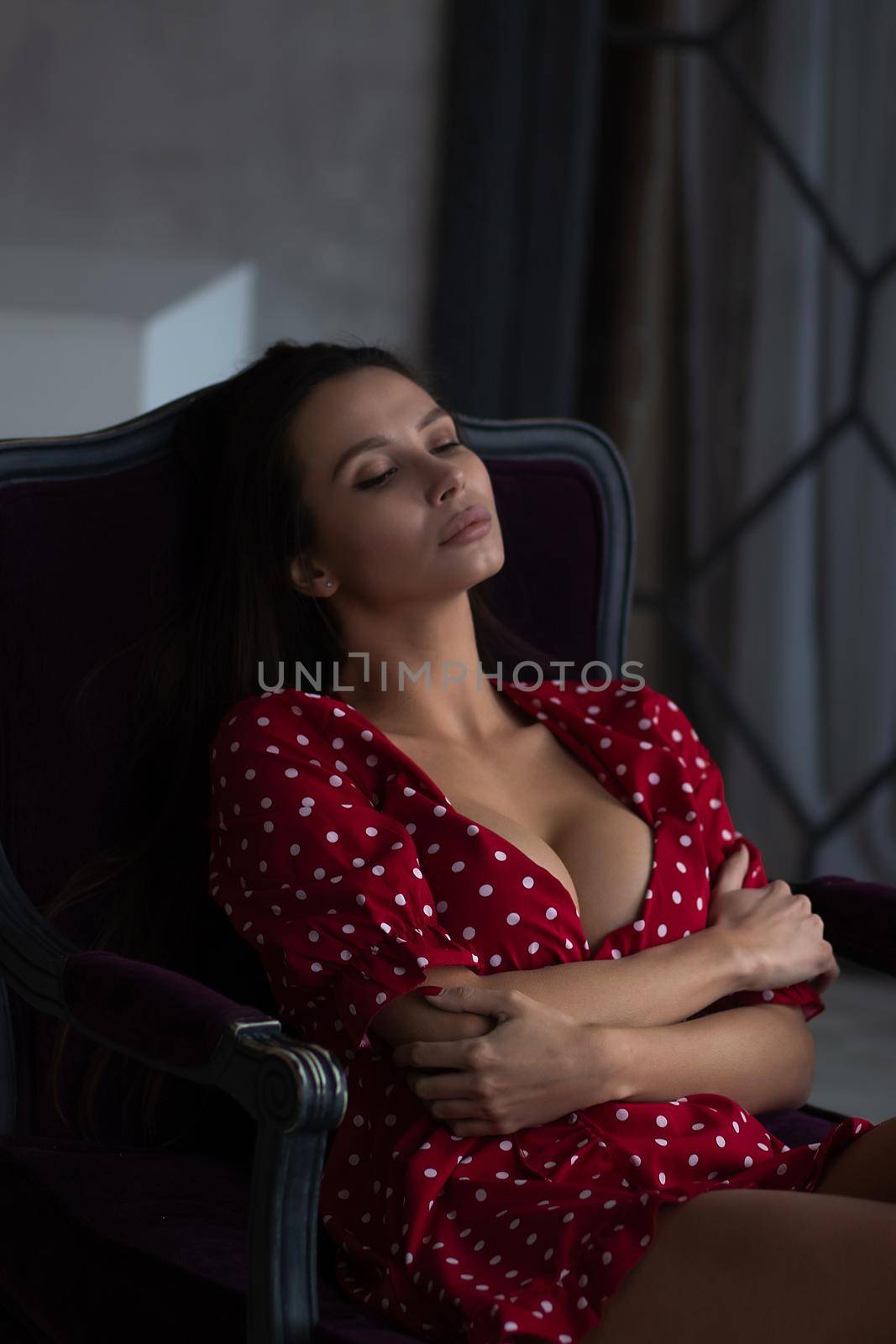 Alluring young woman in feminine dress resting in armchair by 3KStudio