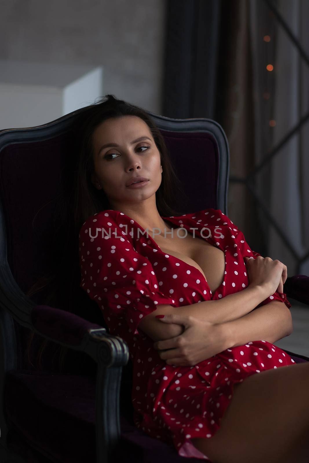 Alluring young woman in feminine dress resting in armchair by 3KStudio