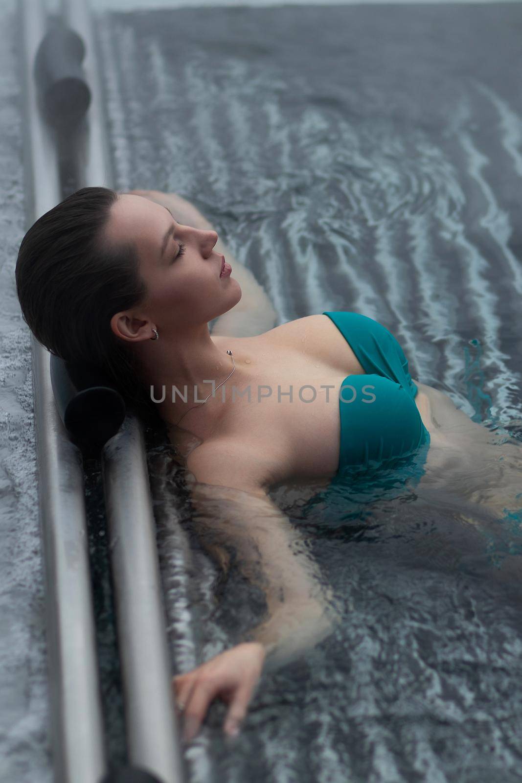 Seductive woman in pink bra crossing arms and looking away while resting in clean water of hot spring on resort